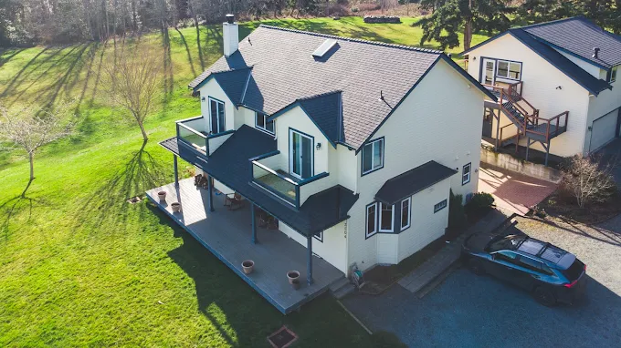 White farmhouse with a new roof and covered deck on a sunny acreage