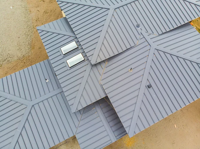 Close aerial view of a grey standing-seam metal roof with skylights